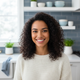 A happy young woman with a genuine smile, looking at the camera in a modern kitchen setting.